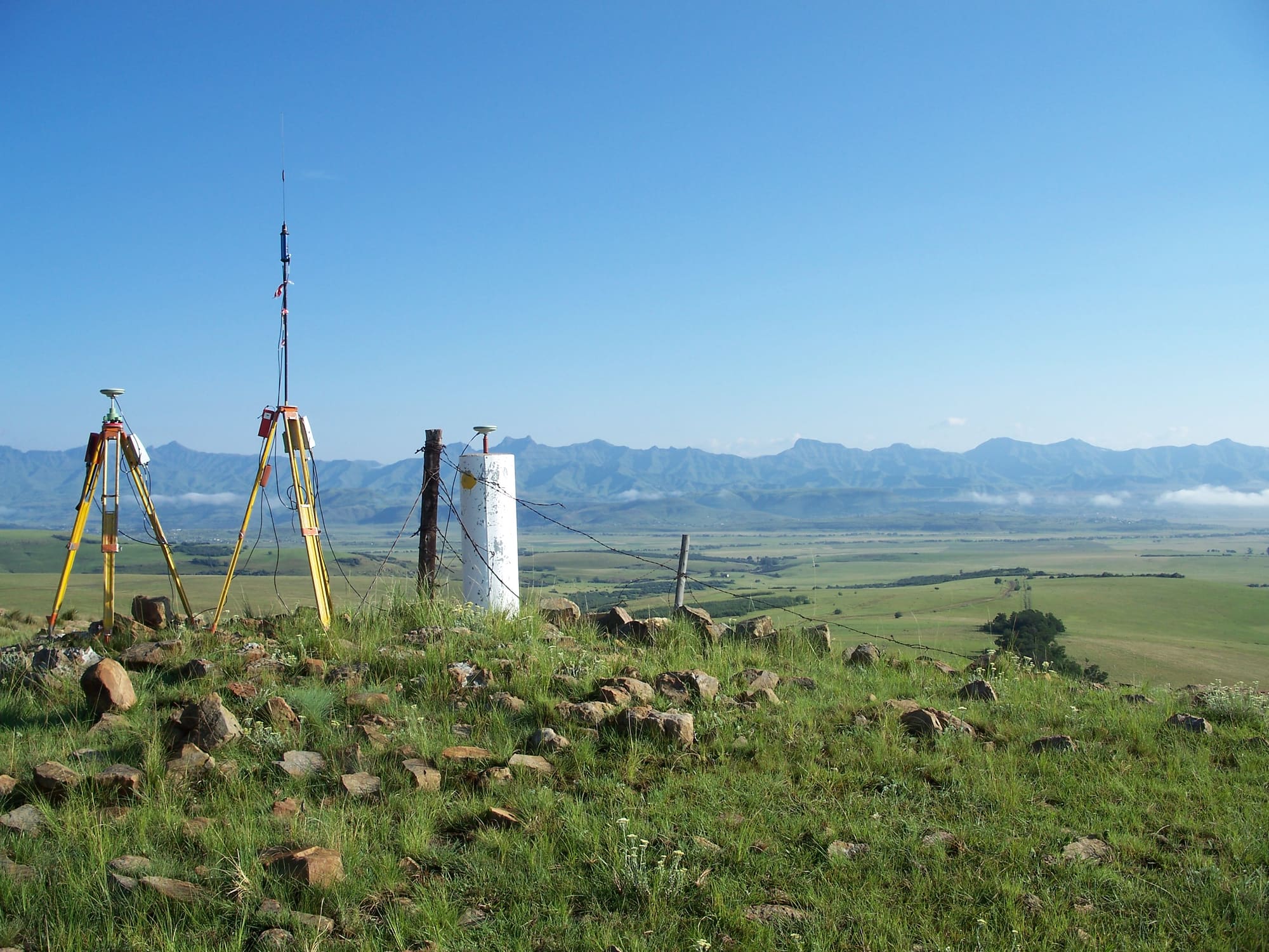 A survey beacon and GNSS equipment on a grassy hillside with mountains behind